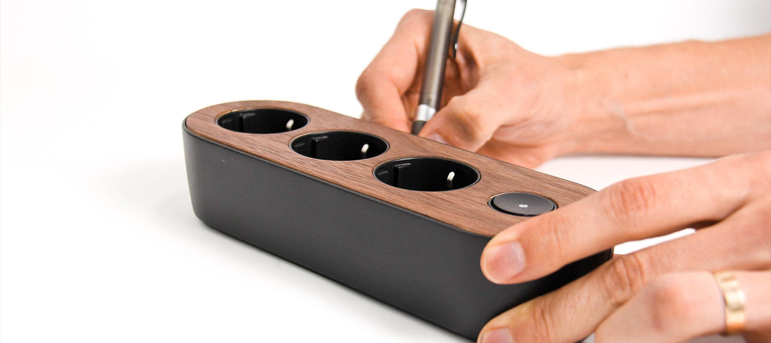 Hand holding black design power strip MyNolla strip black/walnut